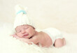 Smiling newborn Caucasian baby boy in bonnet sleeping on a white fur cloth