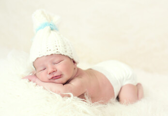 Canvas Print - Smiling newborn Caucasian baby boy in bonnet sleeping on a white fur cloth