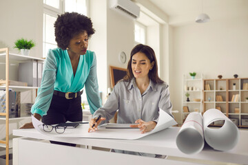 Wall Mural - Two creative architects or modern interior designers working on new project. Young women meeting up in studio office, drawing architectural plan, creating designs and discussing ways to improve them