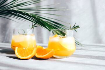 Cocktails with orange slices in glass glasses under the branches of palm trees. Summer drinks. Travel and Leisure