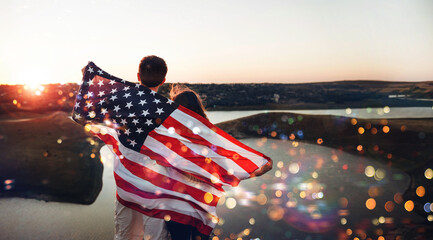 Young family with the American flag behind them at sunset celebrates Independence Day.
 USA celebrate 4th of July. Patriotic holiday.