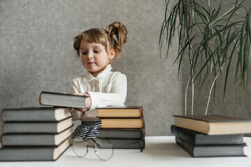 Happy funny baby girl in glasses reading a book. Emotional girl. To school soon