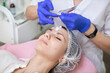 © sofiko14 - Close up top angle view of face of beautiful young woman in disposable hat, having skin cosmetology procedures in modern clinic. Hands of doctor beautician applying cream on client's face