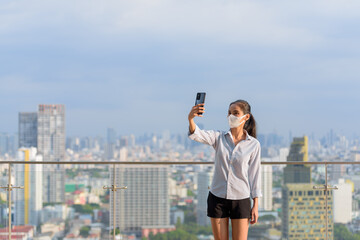 Wall Mural - Woman influencer wearing face mask while using phone and taking selfie or vlogging