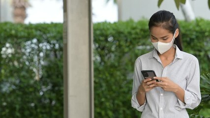 Wall Mural - Woman wearing face mask to protect from coronavirus Covid-19 while using phone and taking selfie outdoors