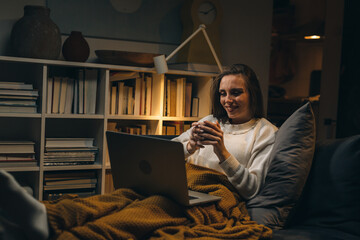 Wall Mural - woman using laptop computer and drinking coffee. she is laying on sofa at home