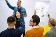 © maxbelchenko - Group of young people sitting at a conference together raised hands to express their views. Business group meeting seminar training concept. Planning, analysis, collaborate work in teamwork.