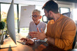 © luckybusiness - A young businessman and elderly female colleague have a conversation about a computer screen content watching together at the desk at workplace. Business, office, job