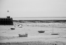 Sailing And Fishing Boats Lying On Sea Floor At Low Tide And A Lighthouse At Small Harbor Near Saint-Malo In The Dusk . Brittany, France. Business On The Rocks /  In Low Water Metaphor. Black White