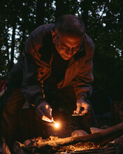 A Man Age 60-70 Lights A Campfire In The Woods