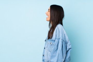 Wall Mural - Young caucasian woman isolated on blue background laughing in lateral position