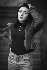 Wall Mural - Grayscale shot of a young Caucasian female wearing coat posing outdoors