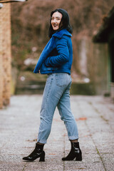 Wall Mural - Young Caucasian female with black hair wearing a black shirt and a blue coat posing outdoors