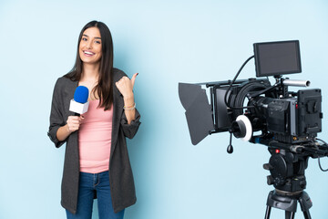 Wall Mural - Reporter woman holding a microphone and reporting news isolated on blue background with thumbs up gesture and smiling