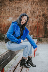 Poster - Young Caucasian female with black hair wearing a black shirt and a blue coat posing outdoors