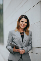 Poster - Young cheerful Caucasian businesswoman in a beautiful formal outfit holding a tablet