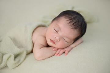 asian newborn baby sleep on green wrap cloth.