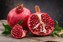 Healthy Pomegranate Fruit With Leaves And Half Of Ripe Pomegranate On A Cutting Board, Side View, Dark Vintage Background.