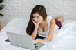 © 220 Selfmade studio - Beautiful Attractive Asian young woman lying on bed and using computer laptop for using social media and shopping online relax in cozy bedroom in holiday,Lifestyle in home Concept