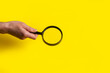 female hand holds a magnifying glass loupe on a yellow background