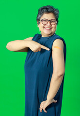 Adult senior Asian woman pointing and smile confident show shoulder with bandage plaster after getting Coronavirus of Covid-19 vaccine injection. Idea for vaccination of population against virus.