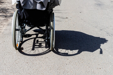 Shadow of the wheelchair and the tires. Shadow of a woman sitting on a wheelchair. Invisible women sitting in wheelchair is shadowed to right. Back of the wheelchair at outdoor shadowed to the right.