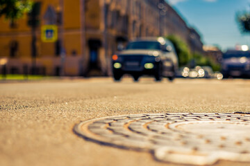 Summer in the city, the car rides down the street with trees. Close up view of a hatch at the level of the asphalt