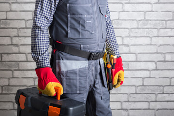 Wall Mural - Repairman ready for work. Service man with toolbox over brick wall background.