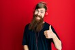 Redhead man with long beard listening to music using headphones doing happy thumbs up gesture with hand. approving expression looking at the camera showing success.