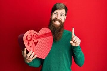 Sticker - Redhead man with long beard holding valentine gift smiling with an idea or question pointing finger with happy face, number one