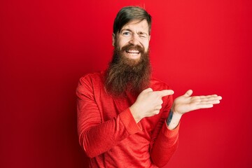 Canvas Print - Redhead man with long beard pointing open palm with finger winking looking at the camera with sexy expression, cheerful and happy face.