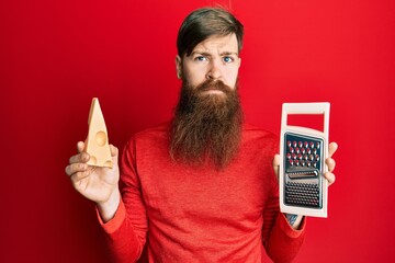 Canvas Print - Redhead man with long beard holding grater and cheese skeptic and nervous, frowning upset because of problem. negative person.