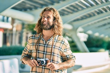 Wall Mural - Young caucasian tourist man smiling happy using vintage camera at the park.