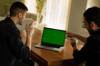 © Alla's StockPhoto - Zwei junge Männer, Anfang 20. sitzen im Wohnzimmer, schauen auf den Display eines Laptops und zeigen mit den Fingern drauf, Einer davon lacht. Green screen, grüner Bildschirm