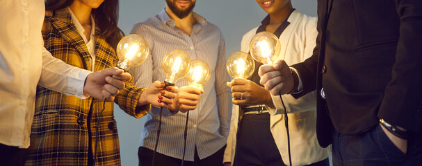 Wall Mural - Background with young multiethnic business team holding glowing vintage Edison lightbulbs. Multiracial men and women join shining electric light bulbs for teamwork and sharing creative ideas