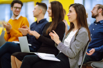 Wall Mural - Young audience sitting in a row and making notes while listening to presentation at conference hall. Business group meeting seminar training concept. Planning, analysis, collaborate work in teamwork.