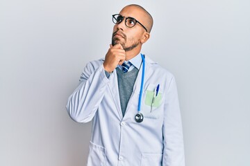 Wall Mural - Hispanic adult man wearing doctor uniform and stethoscope with hand on chin thinking about question, pensive expression. smiling with thoughtful face. doubt concept.