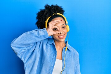 Sticker - Young african american girl listening to music using headphones smiling happy doing ok sign with hand on eye looking through fingers