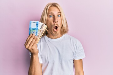 Poster - Caucasian young man with long hair holding hungarian forint banknotes scared and amazed with open mouth for surprise, disbelief face