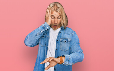 Poster - Caucasian man with blond long hair wearing casual denim jacket looking at the watch time worried, afraid of getting late