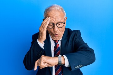 Poster - Senior caucasian man wearing business suit and tie looking at the watch time worried, afraid of getting late