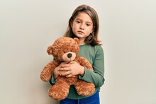 Little Beautiful Girl Hugging Teddy Bear Relaxed With Serious Expression On Face. Simple And Natural Looking At The Camera.