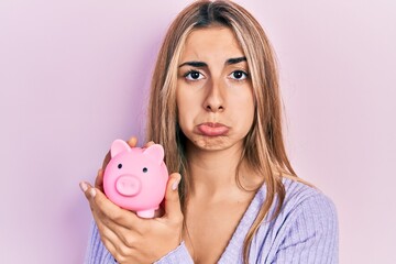 Sticker - Beautiful hispanic woman holding piggy bank depressed and worry for distress, crying angry and afraid. sad expression.