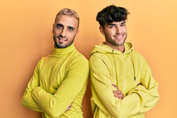 Wall Mural - Homosexual gay couple standing together wearing yellow clothes happy face smiling with crossed arms looking at the camera. positive person.