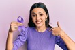 Young hispanic woman holding purple ribbon awareness pointing finger to one self smiling happy and proud