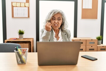 Poster - Middle age businesswoman sitting on desk working using laptop at office angry and mad raising fist frustrated and furious while shouting with anger. rage and aggressive concept.