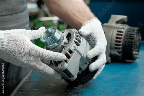 Car spare parts.New generator close-up in the hands of a mechanic.There\'s a faulty generator in the background.Monitoring of spare parts before replacing them and installing them during engine repairs