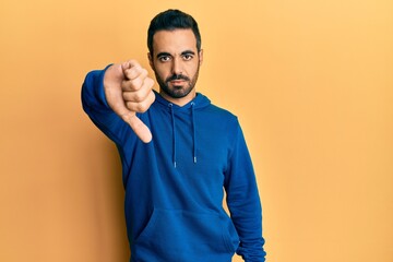 Poster - Young hispanic man wearing casual clothes looking unhappy and angry showing rejection and negative with thumbs down gesture. bad expression.