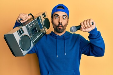 Poster - Young hispanic man holding boombox, listening to music singing with microphone making fish face with mouth and squinting eyes, crazy and comical.