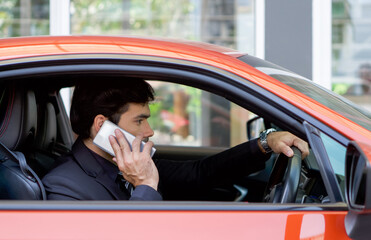 Young businessman in a black suit using mobile phone while holding the car wheel.